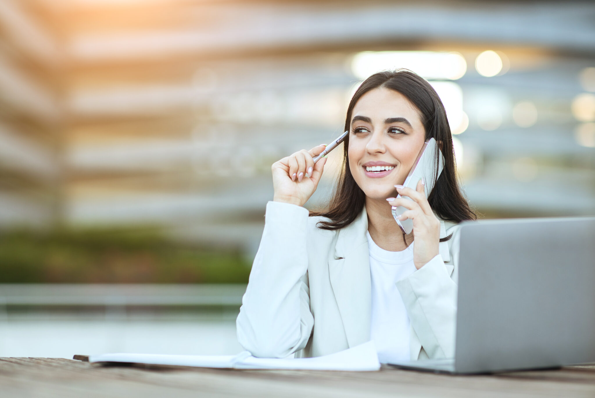 businesswoman working on laptop and talking on cell phone outside